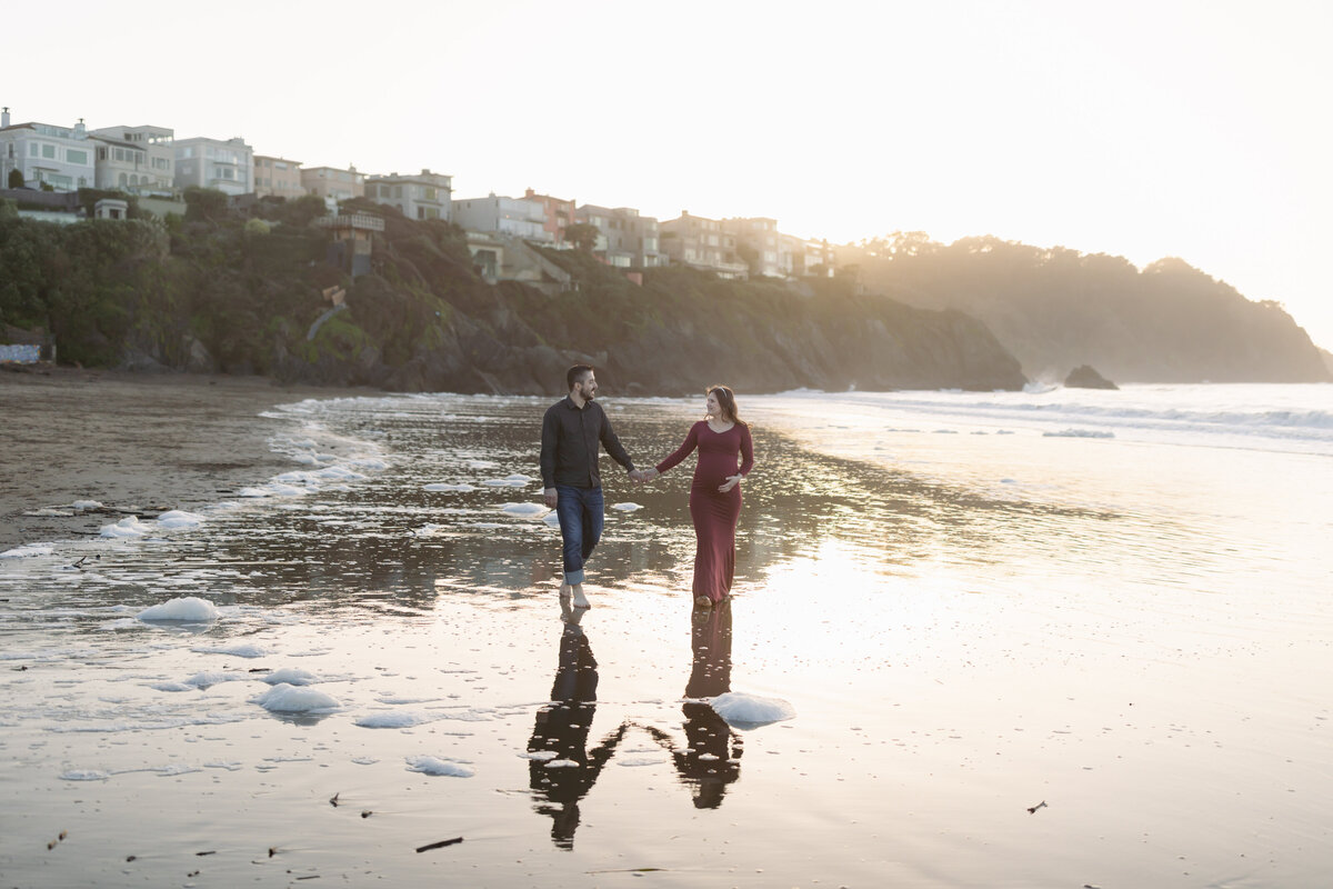 man and woman holding hands walking along the coastline