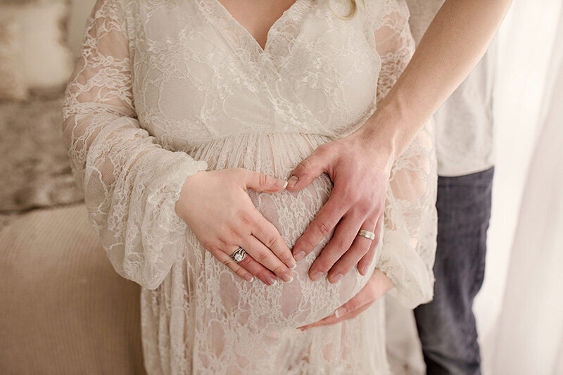 A couple holding heart hands over a baby bump in a Medina Ohio photography studio
