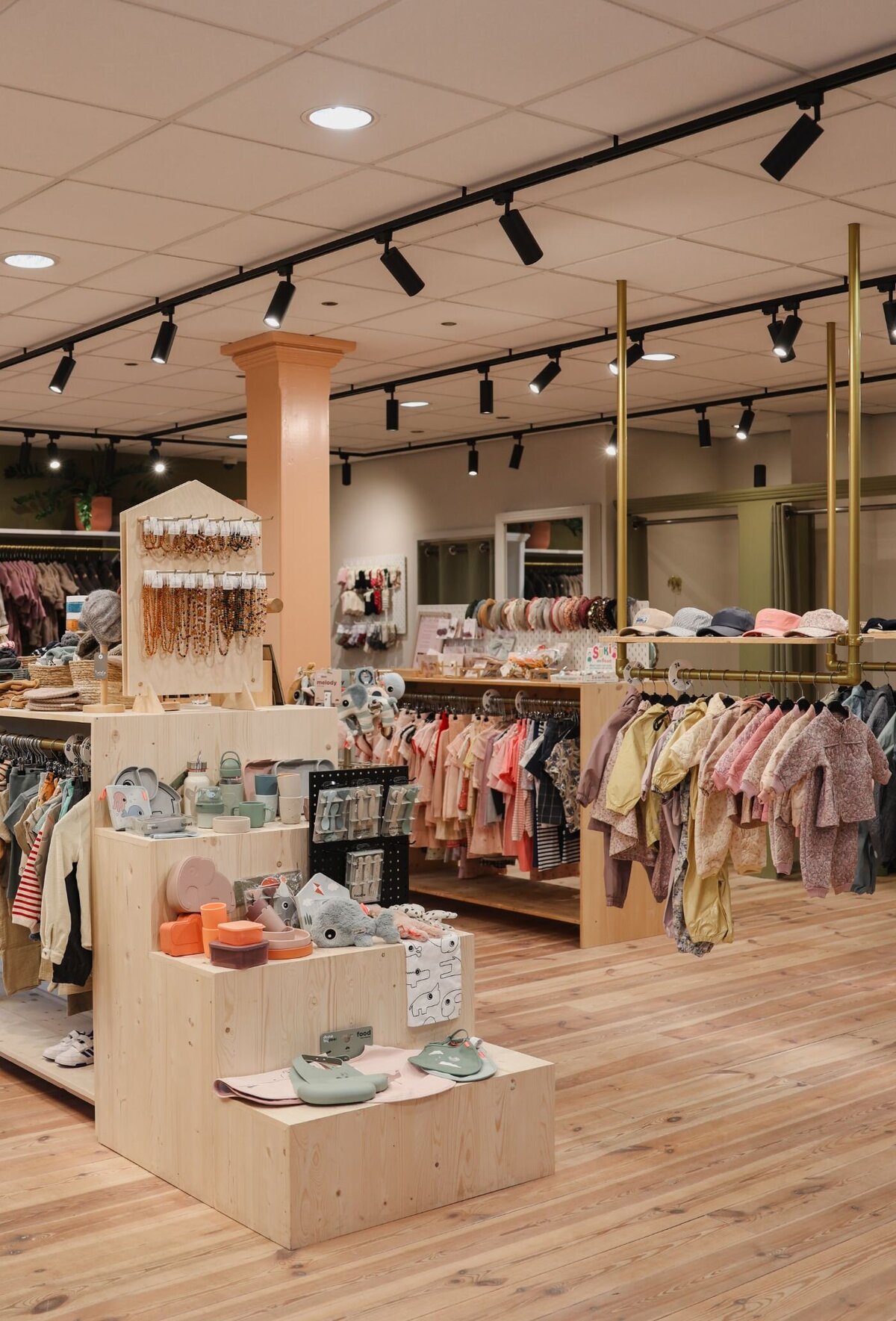 Overzicht van een lichte, moderne kinderwinkel met houten vloer, kledingrekken, sieraden en speelgoed.