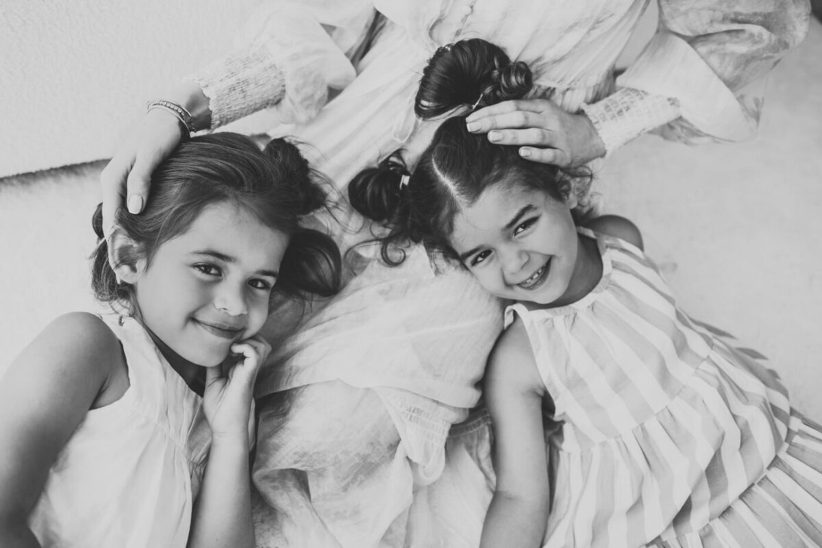 a black and white photo with two girls laying down down to their mom’s lap and smiling.