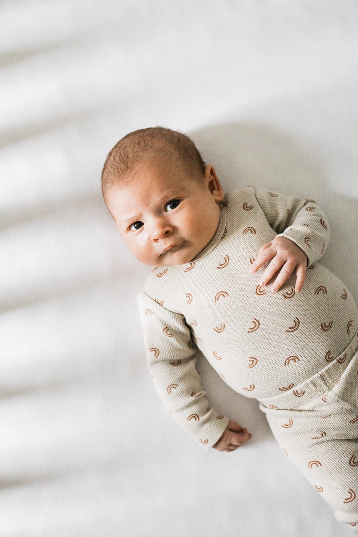 Infant lying on a white blanket wearing a patterned onesie, captured beautifully using DIY newborn photos techniques.