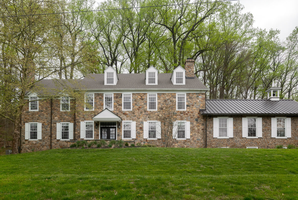 stone house with windows that have white panels with grass front yard