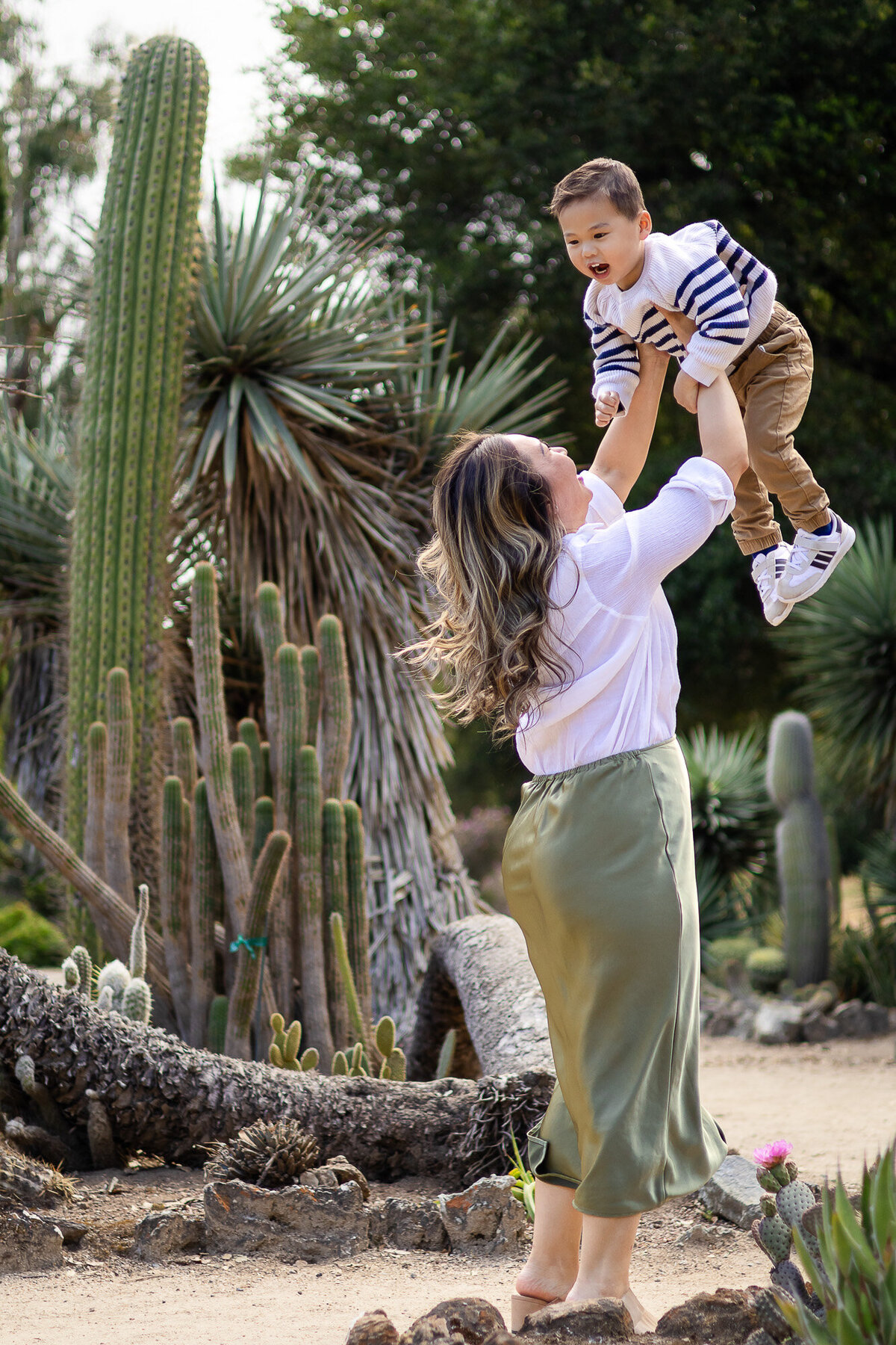 Mother lifting son into the air surrounded by towering cactus plants – Bay Area Family Portfolio - Ellobelle Photography.