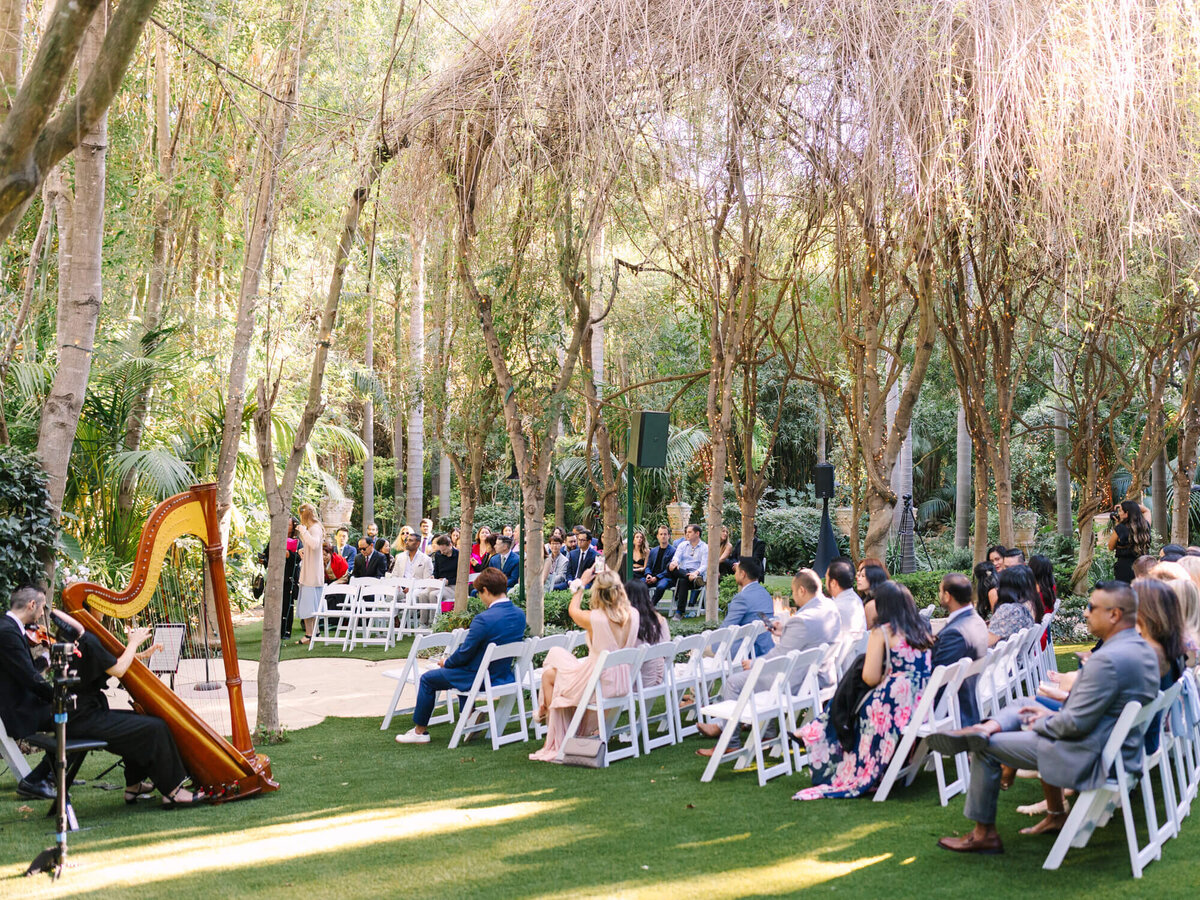A serene outdoor wedding ceremony at Hartley Botanica with guests seated on white chairs under a canopy of trees.