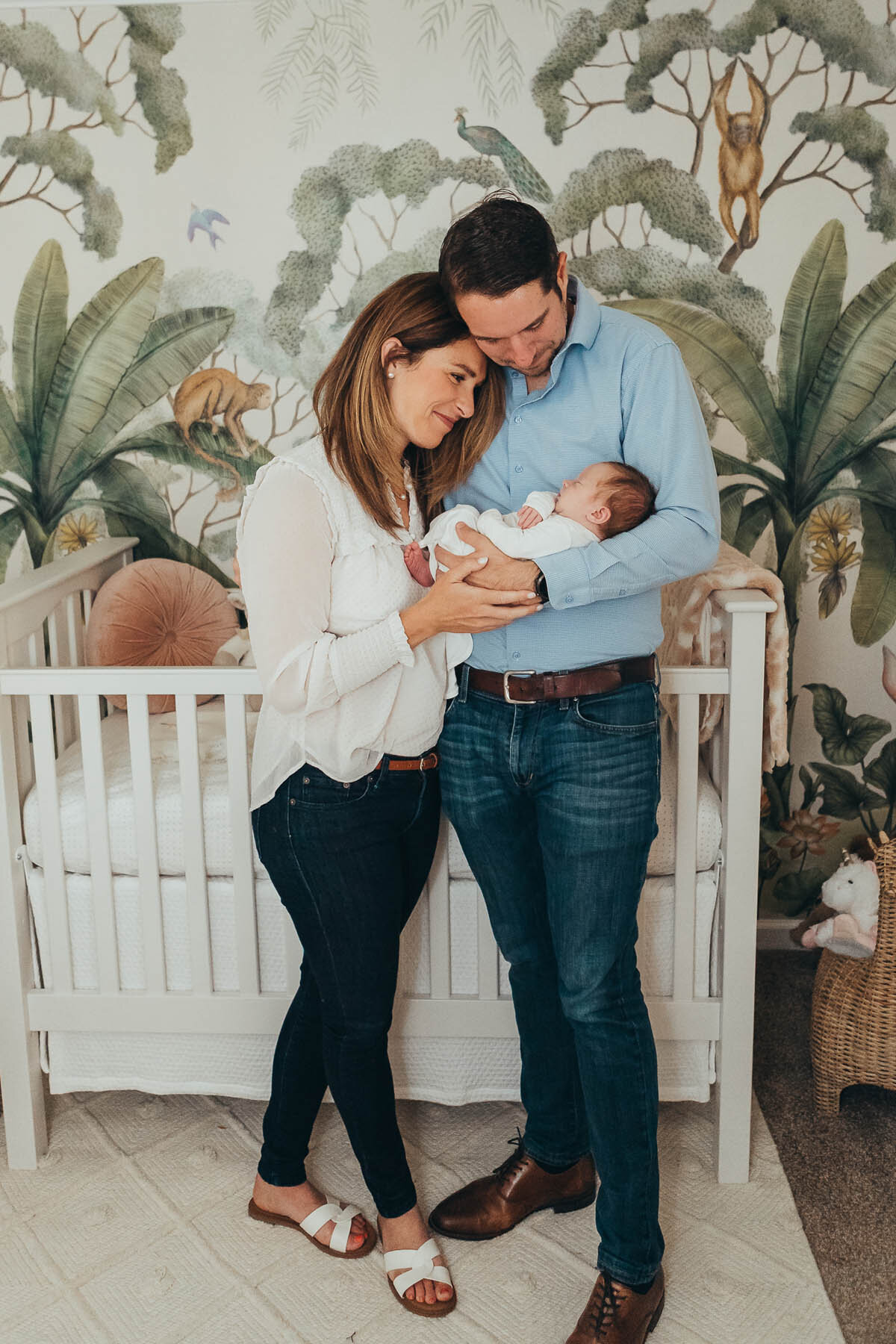 mom and dad stand in front of their baby's crib and hold their baby while they look at him