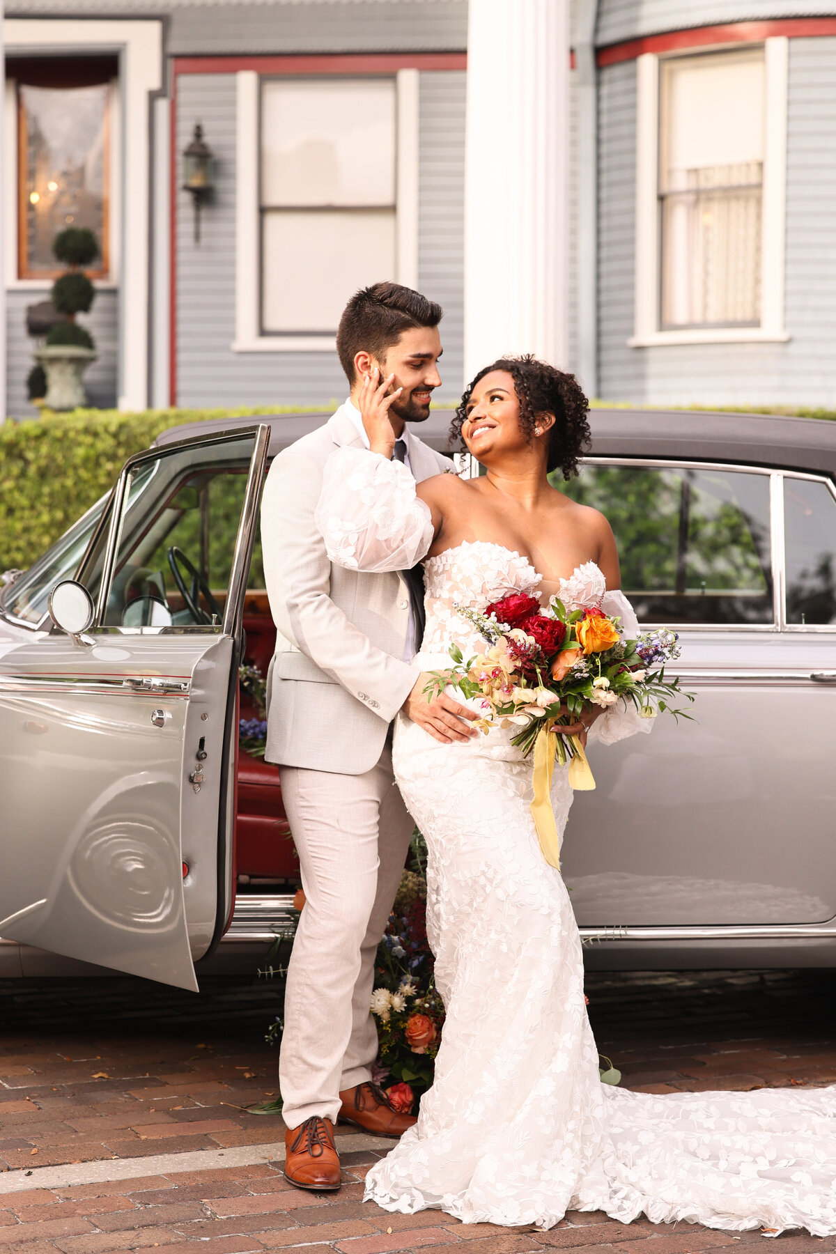 bride wearing lace dress and groom wearing  tan suit standing in front of gray vintage car