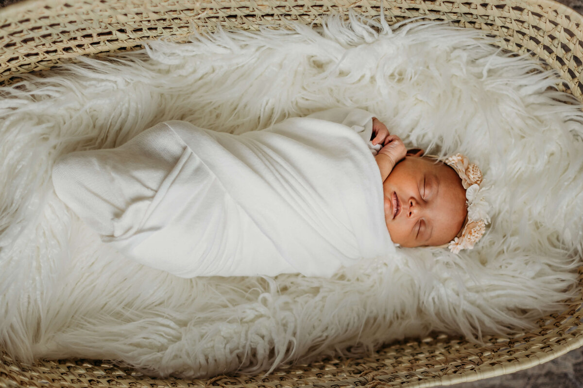 sleeping newborn baby girl with flower crown in white swaddle in basket near eau claire wi