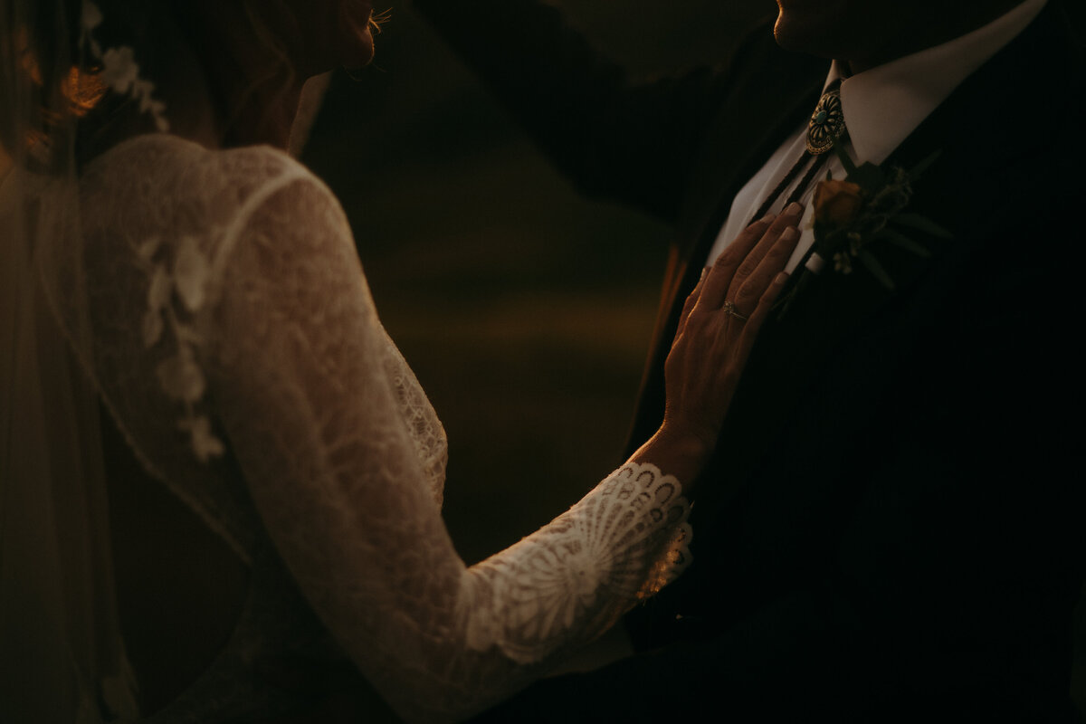 Bride and groom standing together. The bride has her hand on the grooms chest. Zoomed in close to only show the torsos