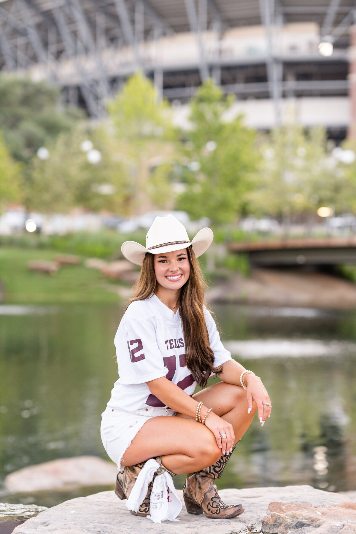 Texas A&M senior girl kneeling down on rocks and smiling at Aggie Park in front of Kyle Field