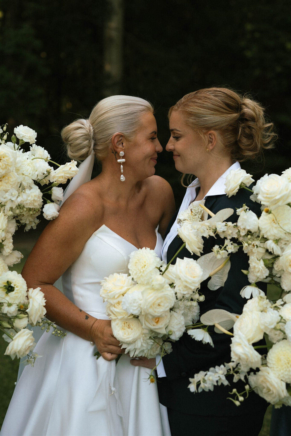 lesbian wives couple with white florals looking at each other on wedding day