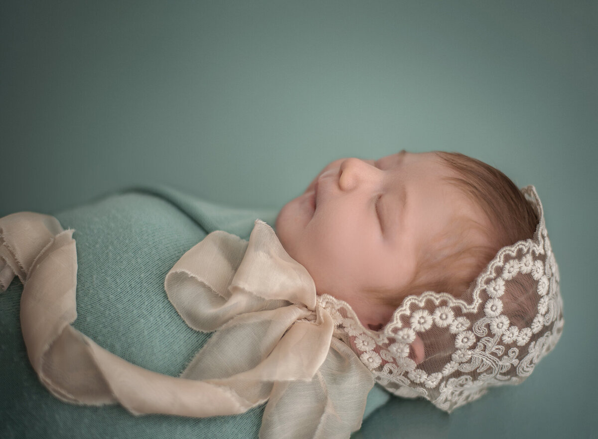 baby girl with lace bonnet on seafoam green background