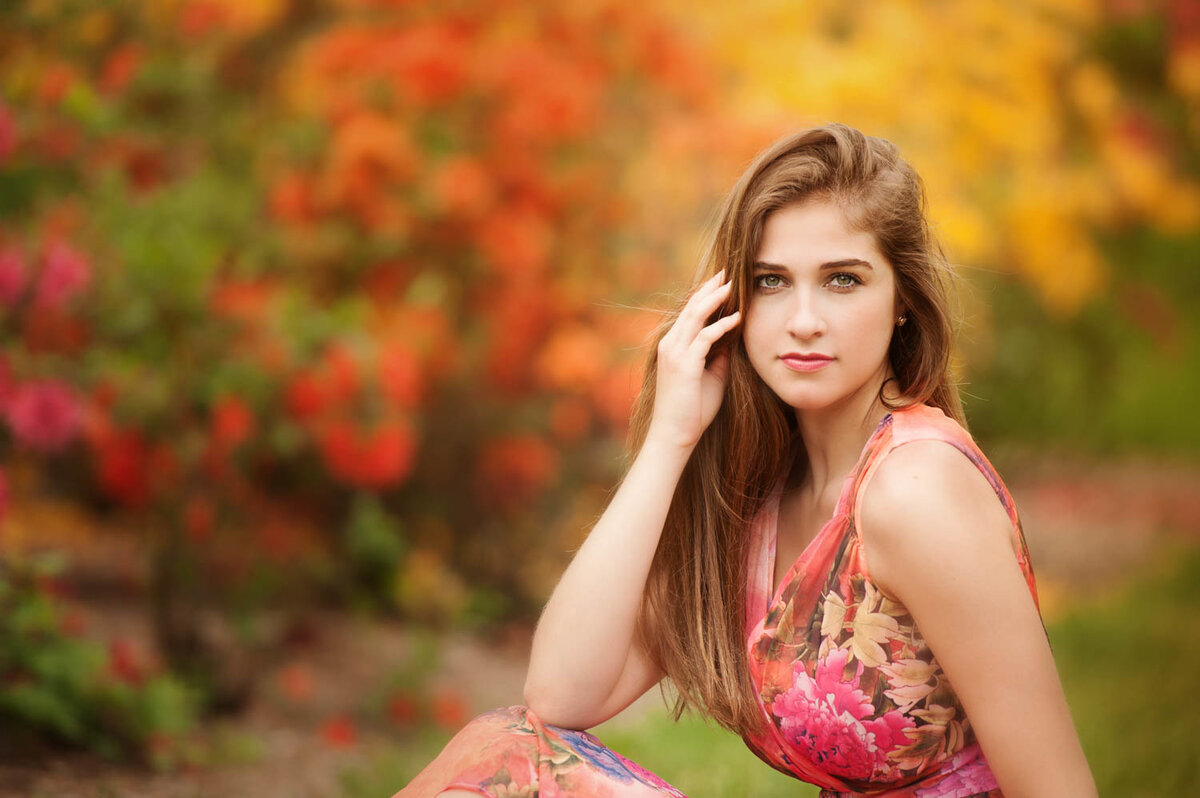 high school senior photo of girl in floral print dress in front of blooming trees in spring