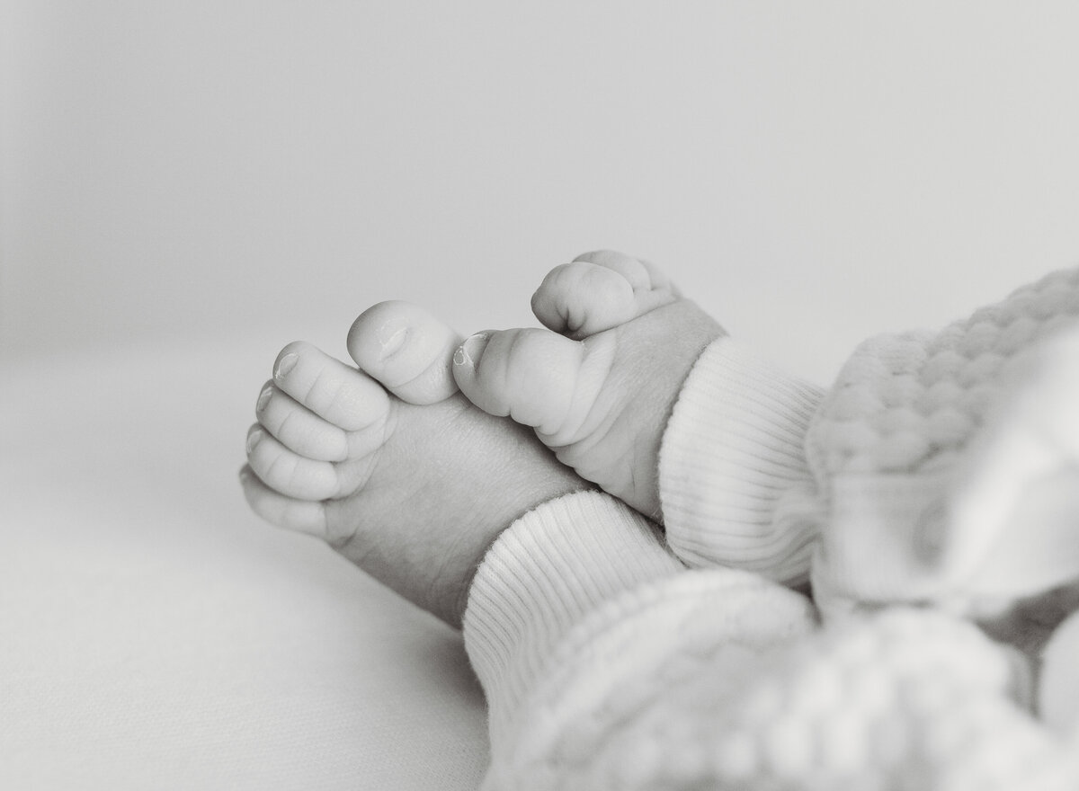 Black and white close-up of tiny newborn feet and hands, highlighting delicate baby details.