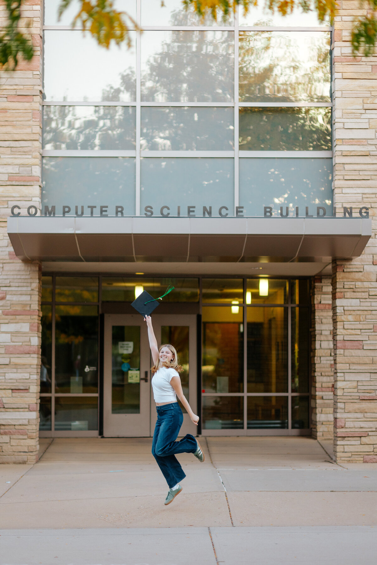 A Colorado State University graduate leaps joyfully in front of the Computer Science Building.