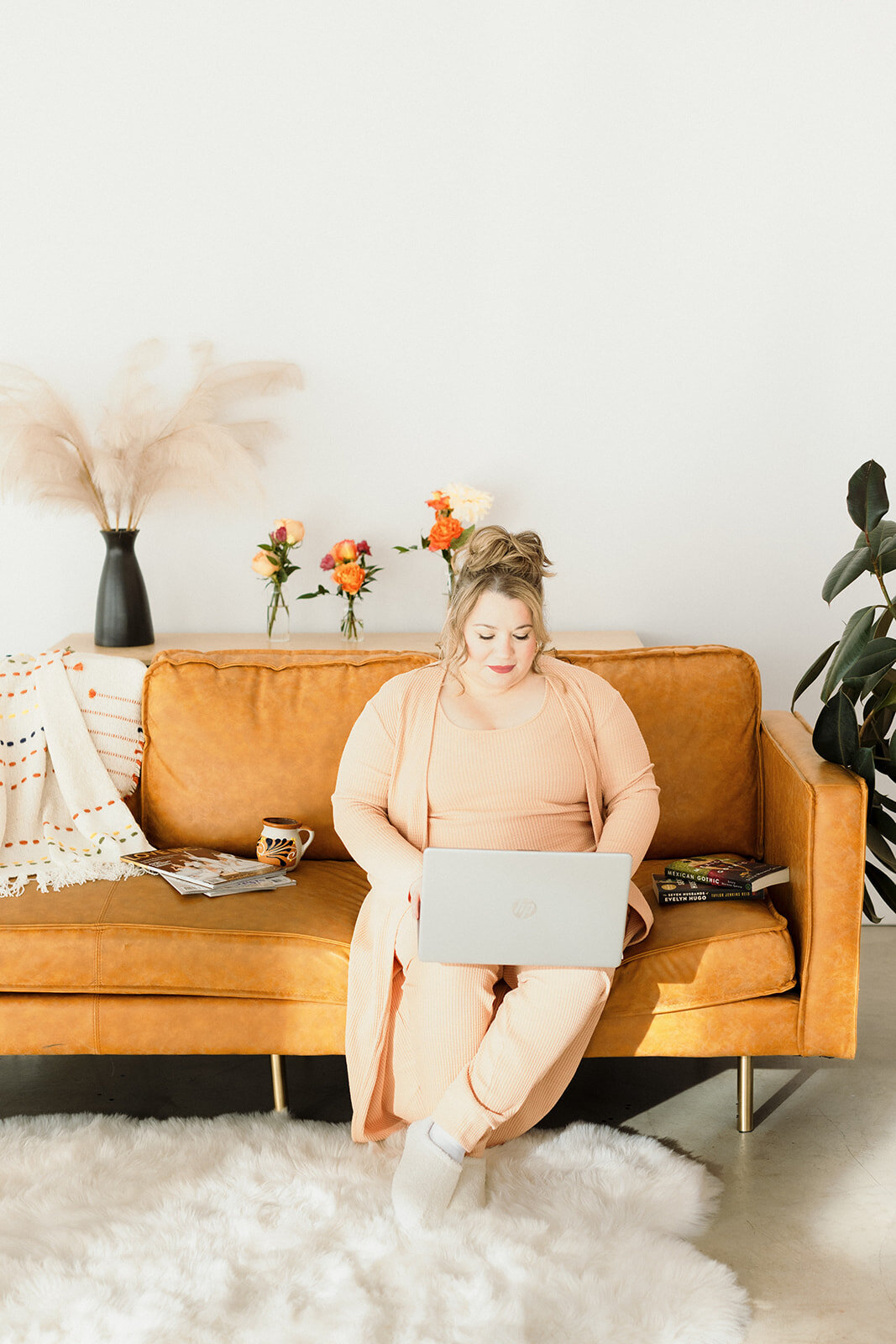 woman in athleisure sitting on orange couch working on her laptop