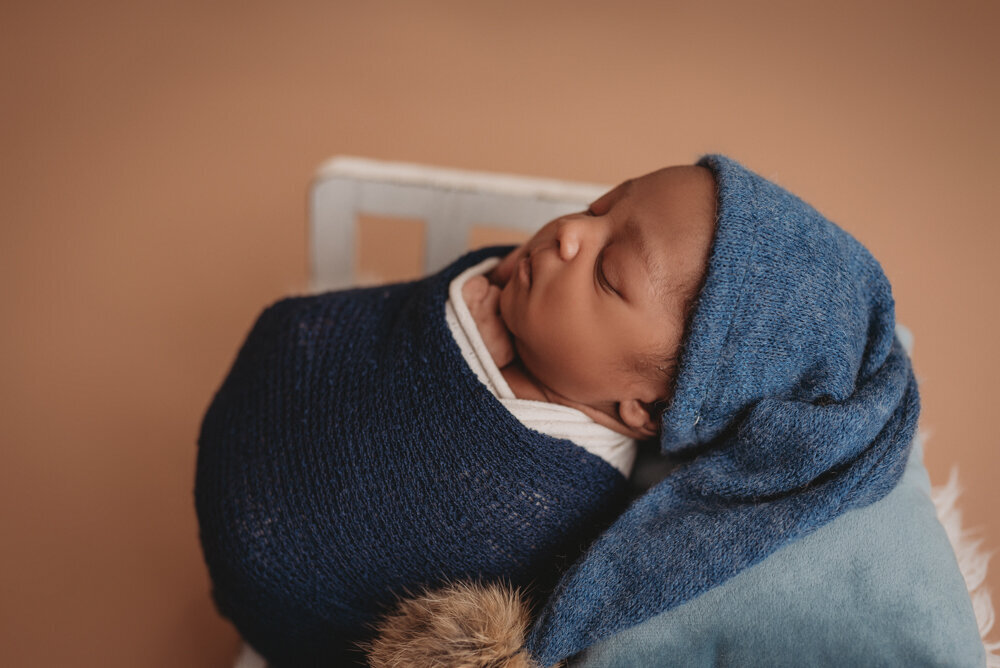Newborn photos with Atlanta, Georgia newborn photographer of sleeping baby boy with hands under chin wearing blue sleepy cap.