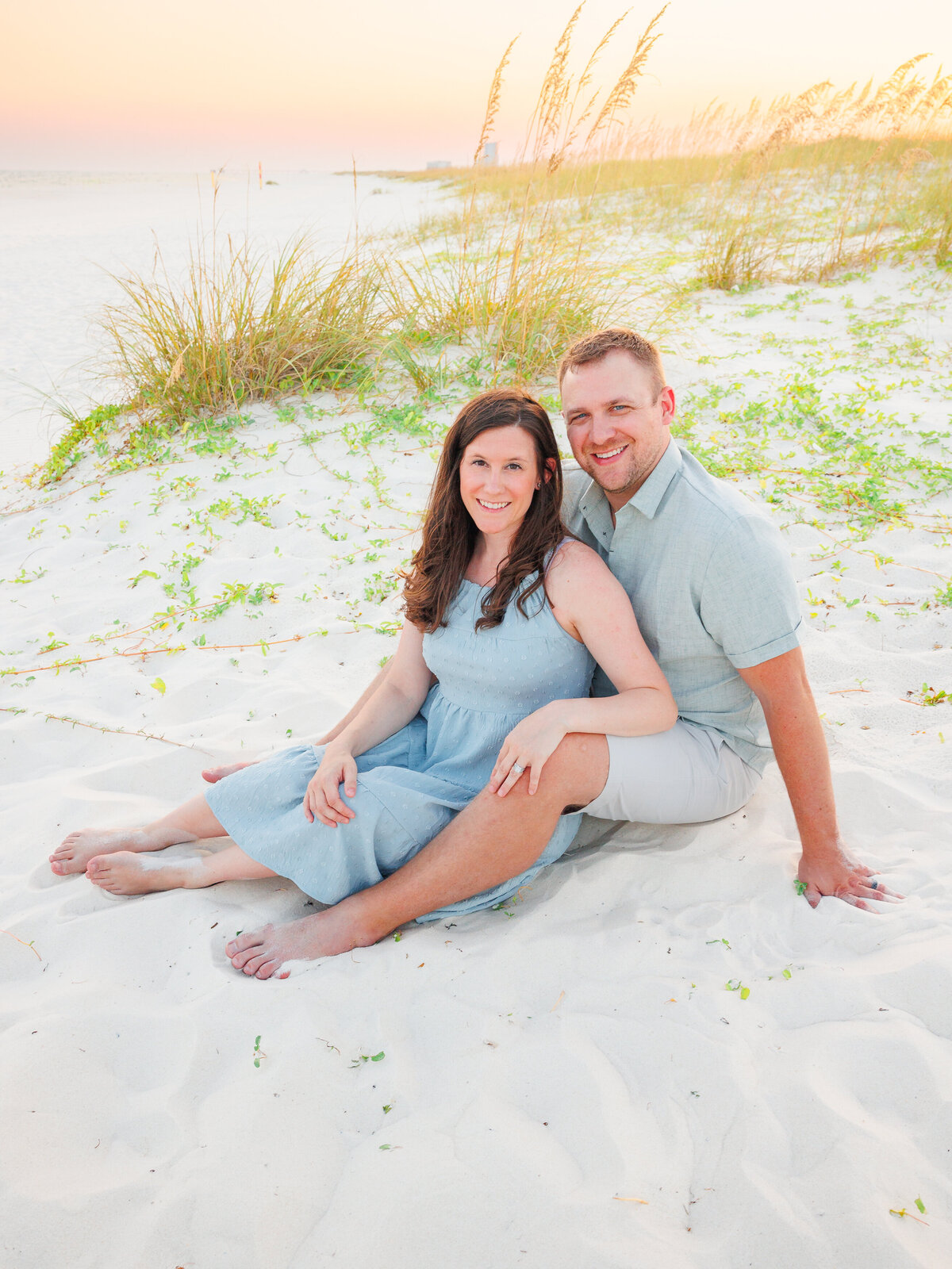 Sitting pose for couple on sand dunes with sunset in the horizon
