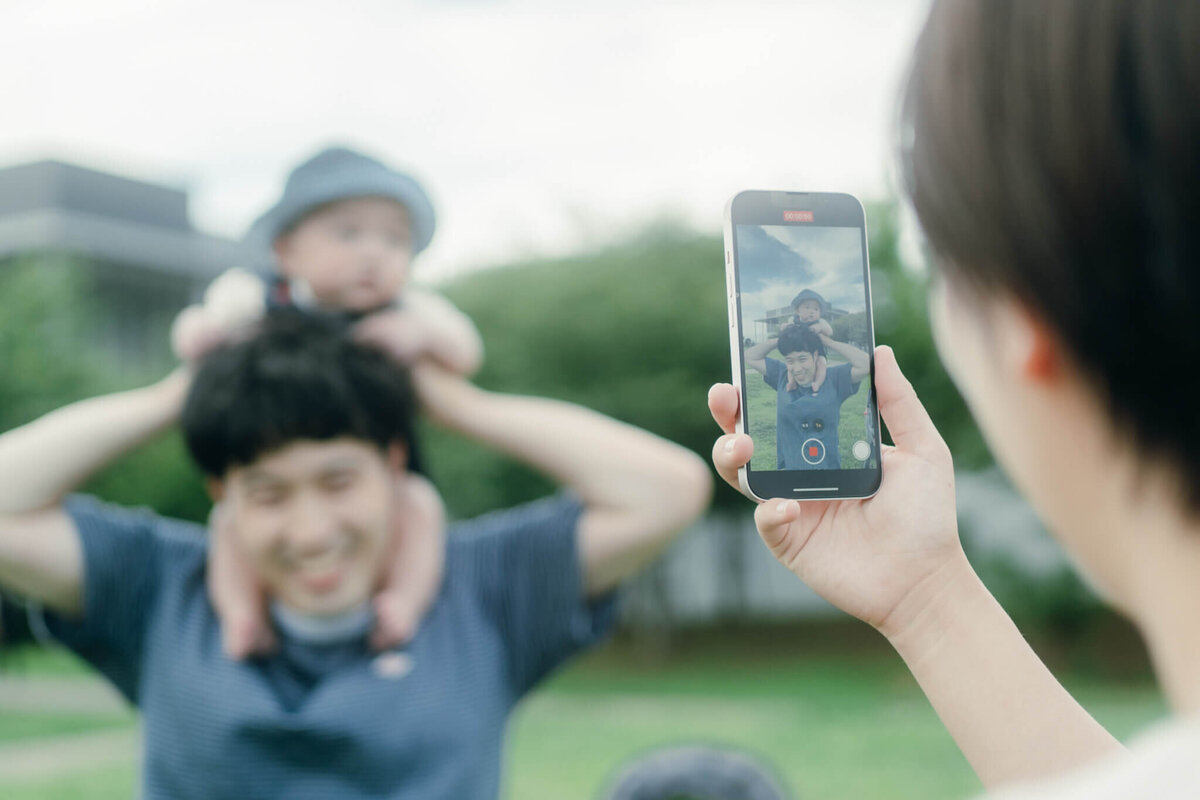 肩車している父と子をスマホで撮影しているところ