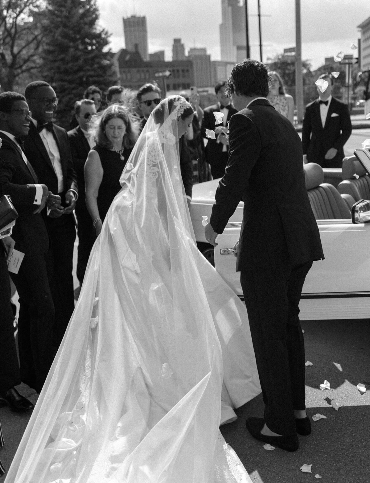 a bride in a long veil is helped into a vintage mercedes convertible by her husband in Detroit, Michigan