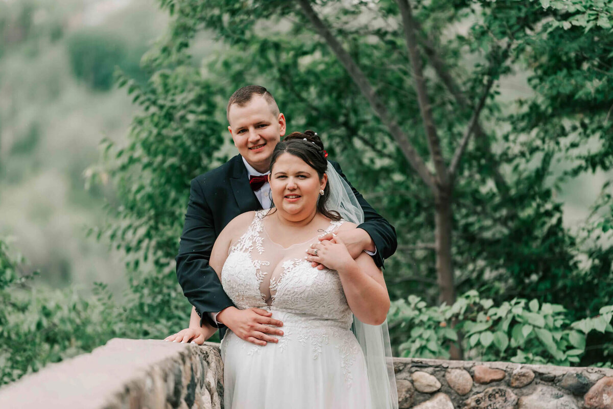 Bridal couple standing  on a path. Groom has his arms wrapped around his bride.