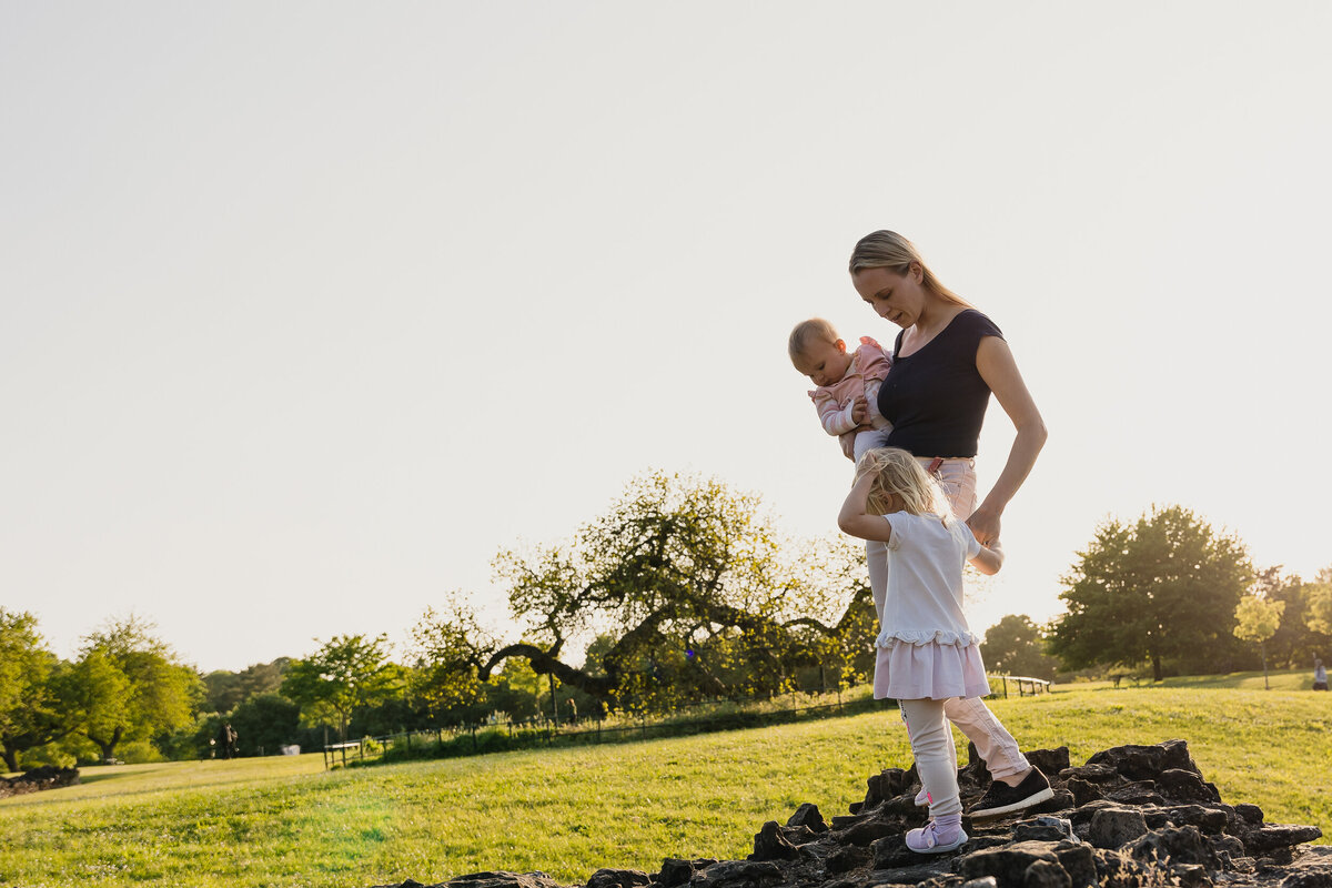 A mother and daughter posing for a photography session on top of a rock in a park.