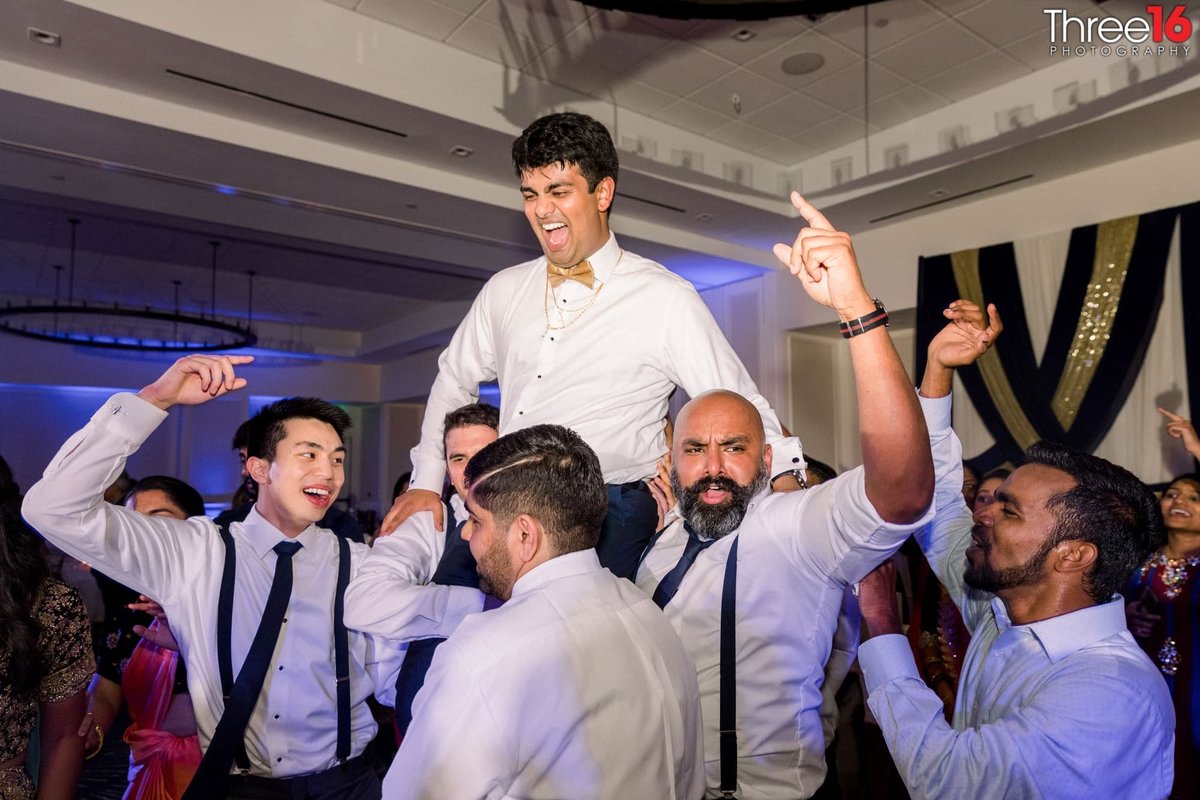 Male guests lift and carry the Groom in the air