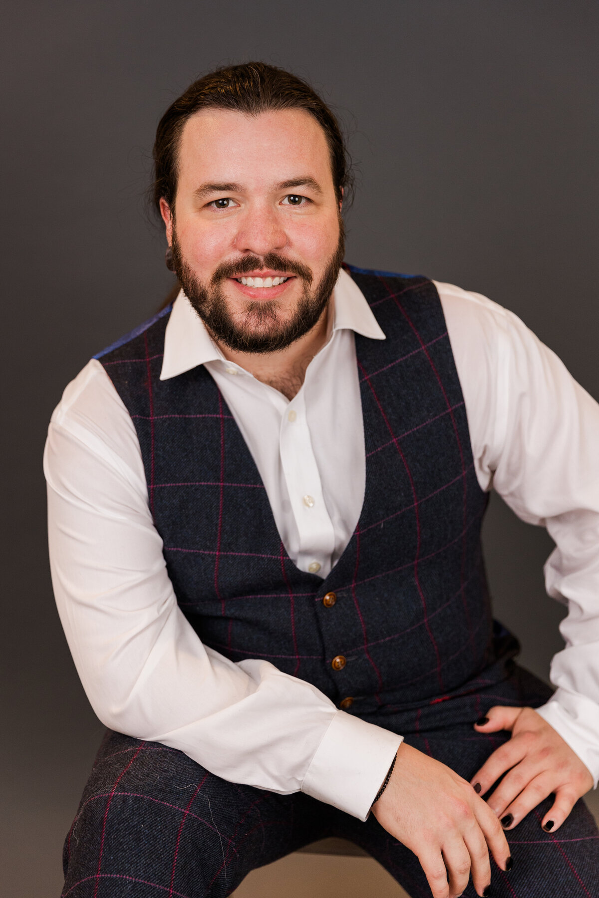man wearing a white shirt and a verst sitting in front of a dark gray backdrop  during portraits in studio