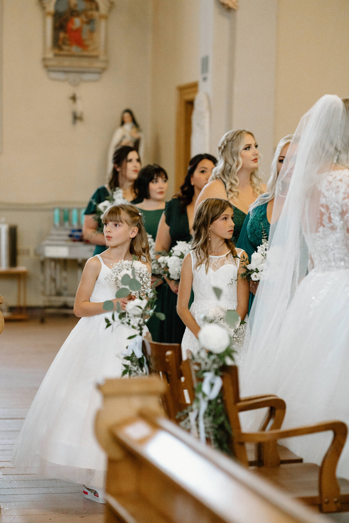 Two young girls in white dresses, holding bouquets as they watch the wedding