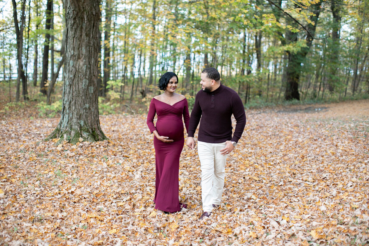 Pregnant couple walk hand in hand in a field of leaves