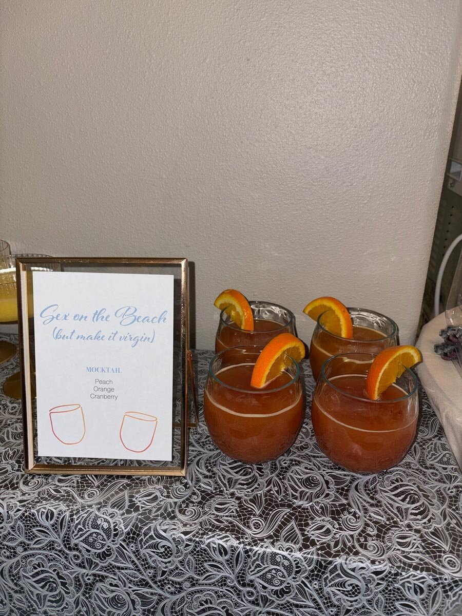 custom bachelorette mocktail sign in floating gold glass frame next to pink drinks garnished with orange