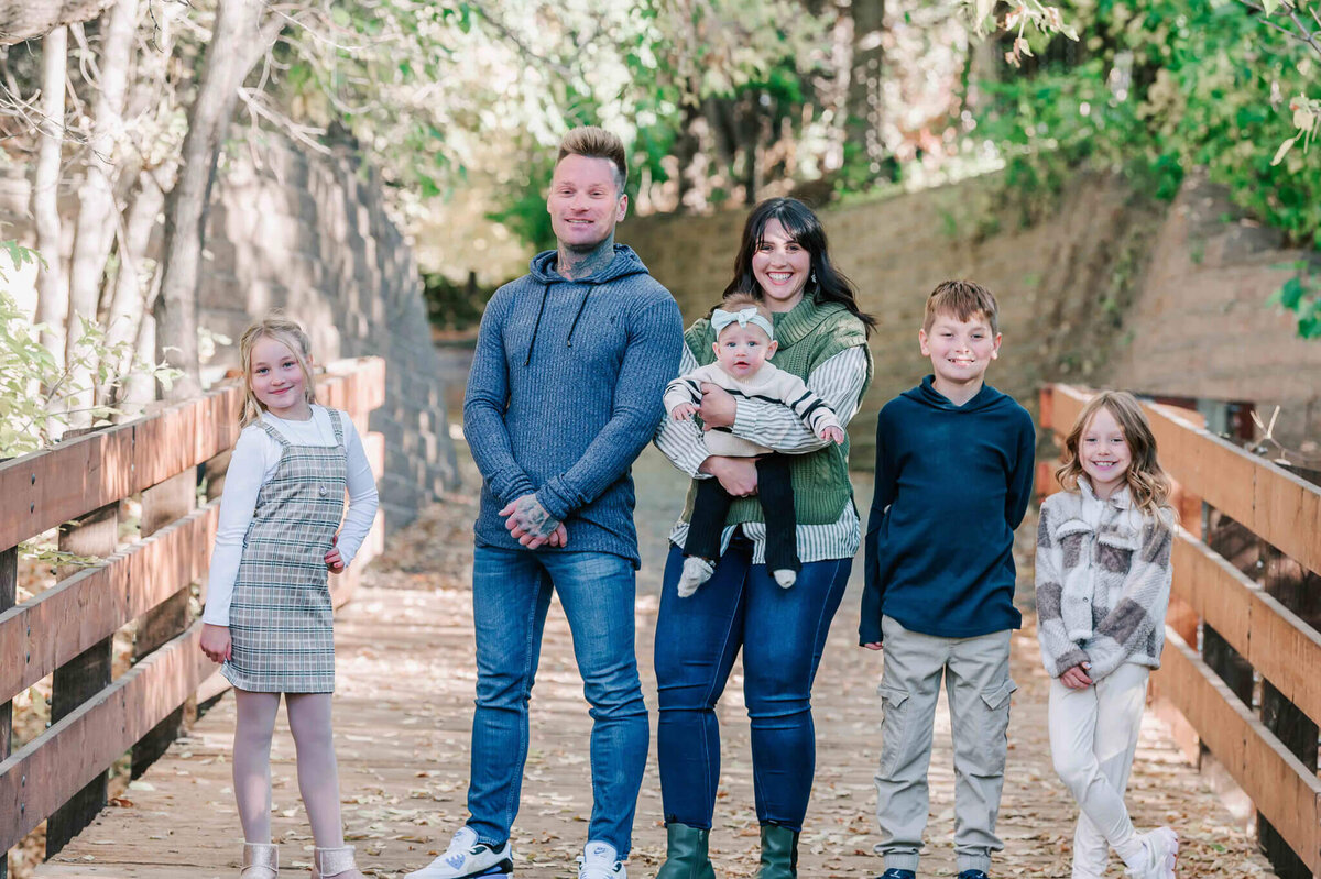 Family standing side by side standing on the edge of a bridge and on a path. 