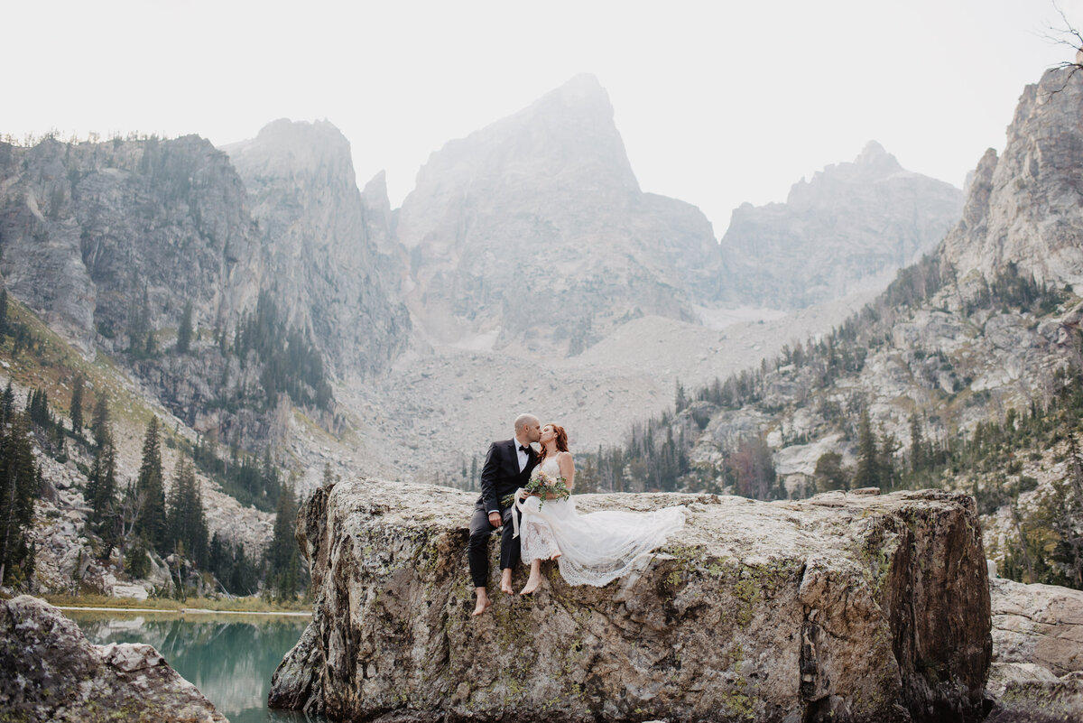 Jackson Hole Photographers capture couple sitting on rock kissing in Grand Tetons