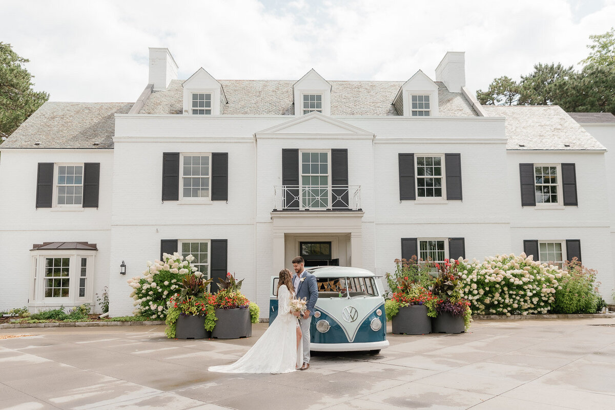 cinematic shot of bride and groom standing in front of a large white mansion