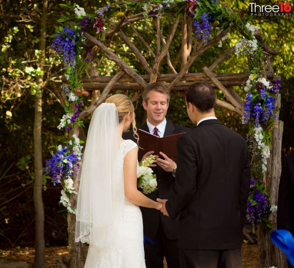 Bride and Groom stand at the altar holding hands while facing the officiant