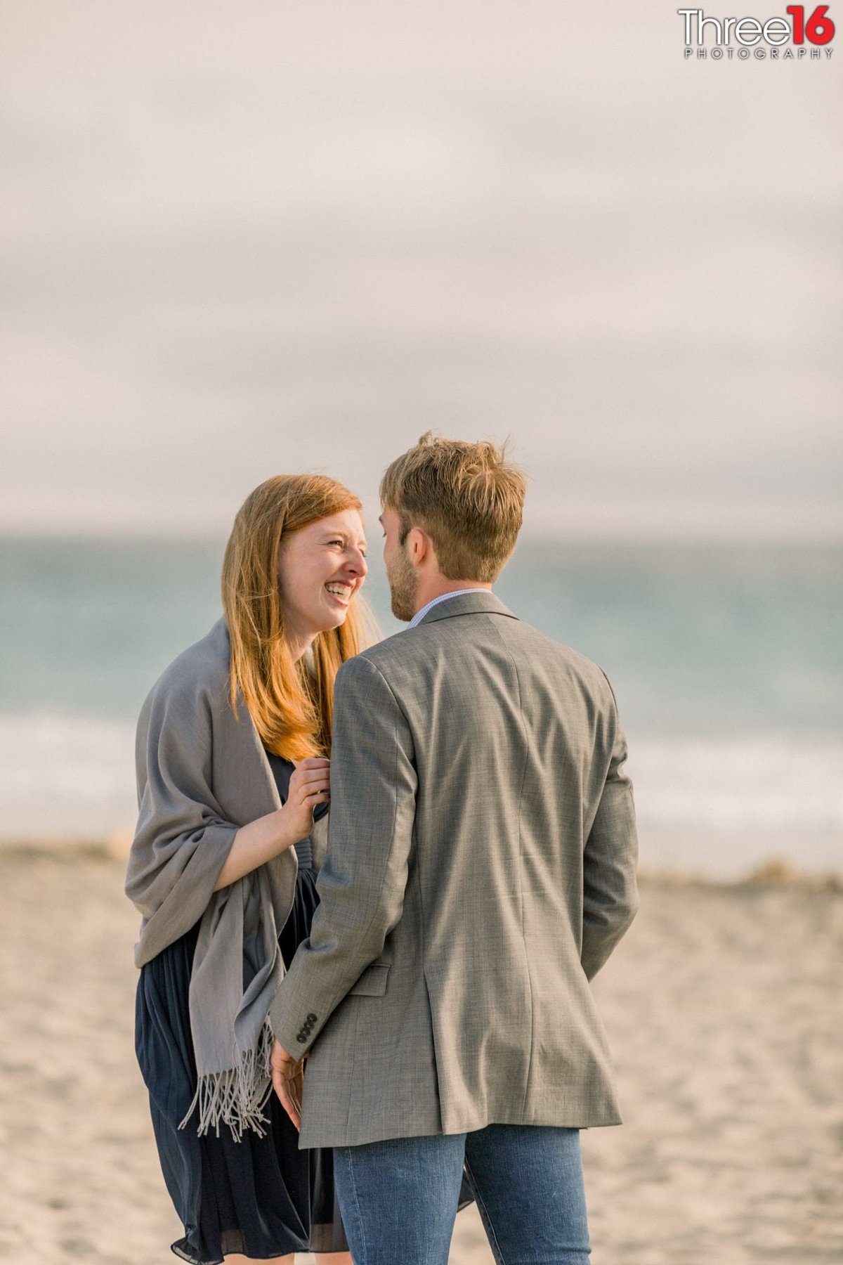 Engaged couple smile together on the beach