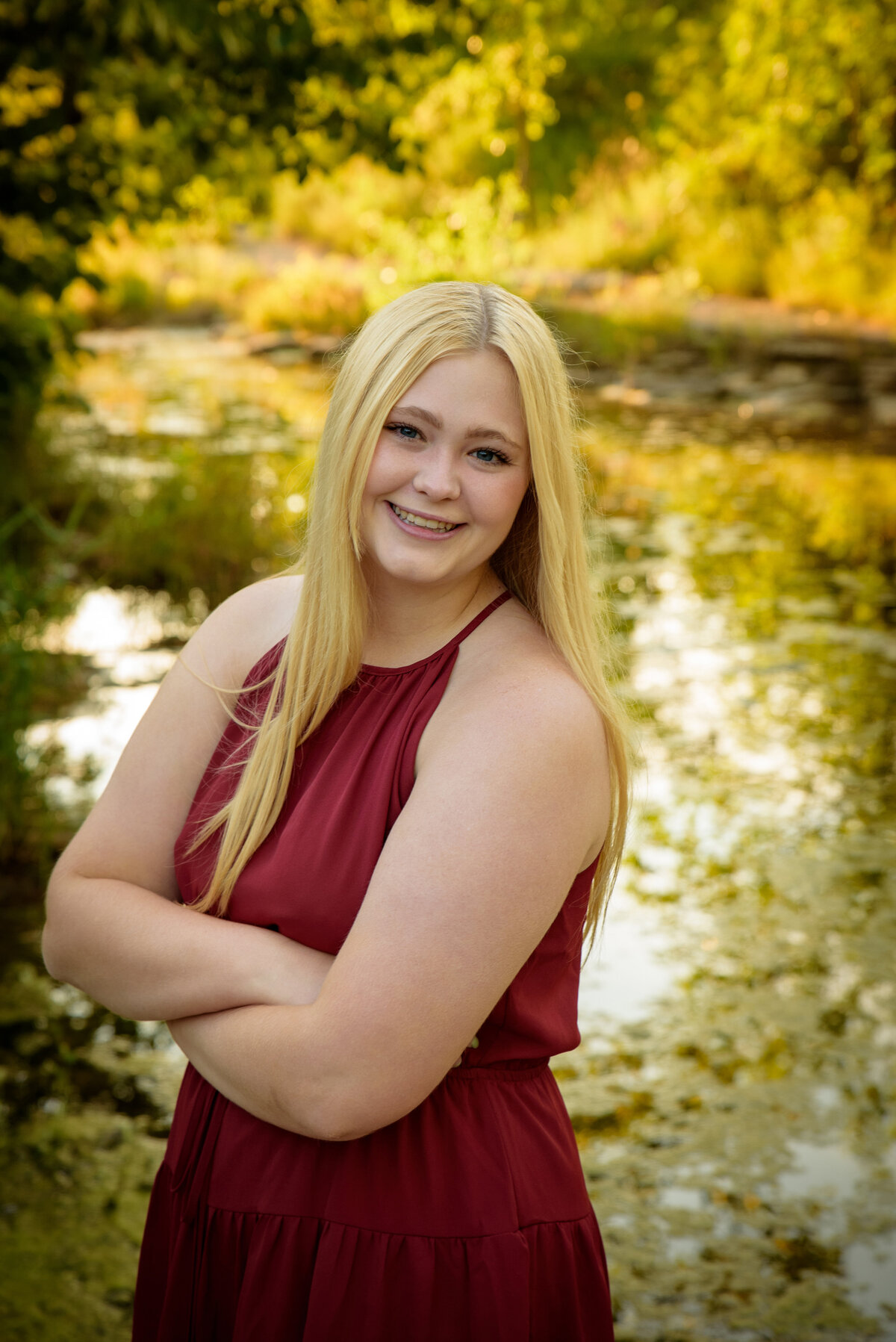 Young woman with long blonde hair wearing a maroon dress standing near the creek at Fonferek Glen County Park near Green Bay, Wisconsin