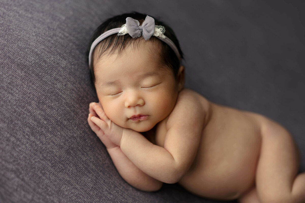 newborn baby girl  laying on her side on a purple backdrop with matching headband and a at a baby photo shoot in Northern VA