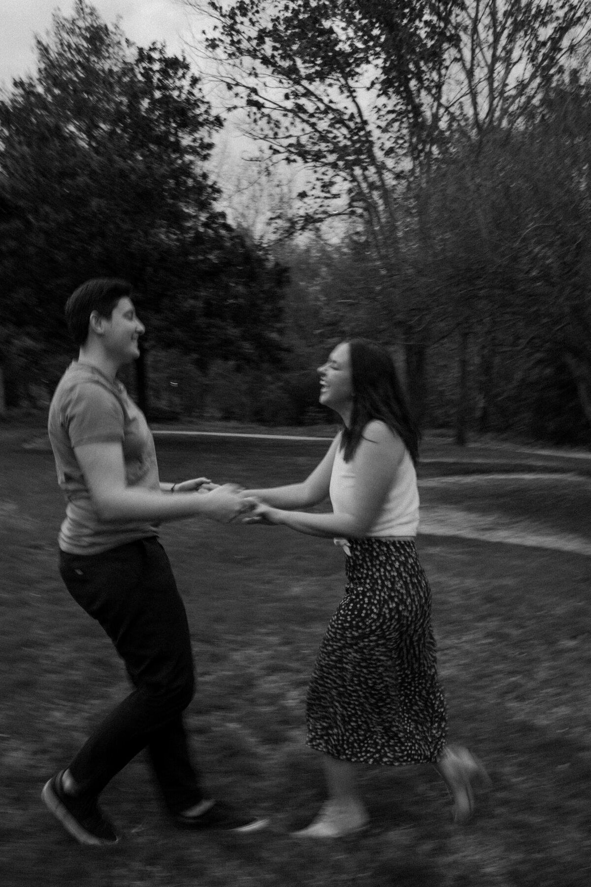 A black and white image capturing a carefree couple dancing in an open field, with blurred motion