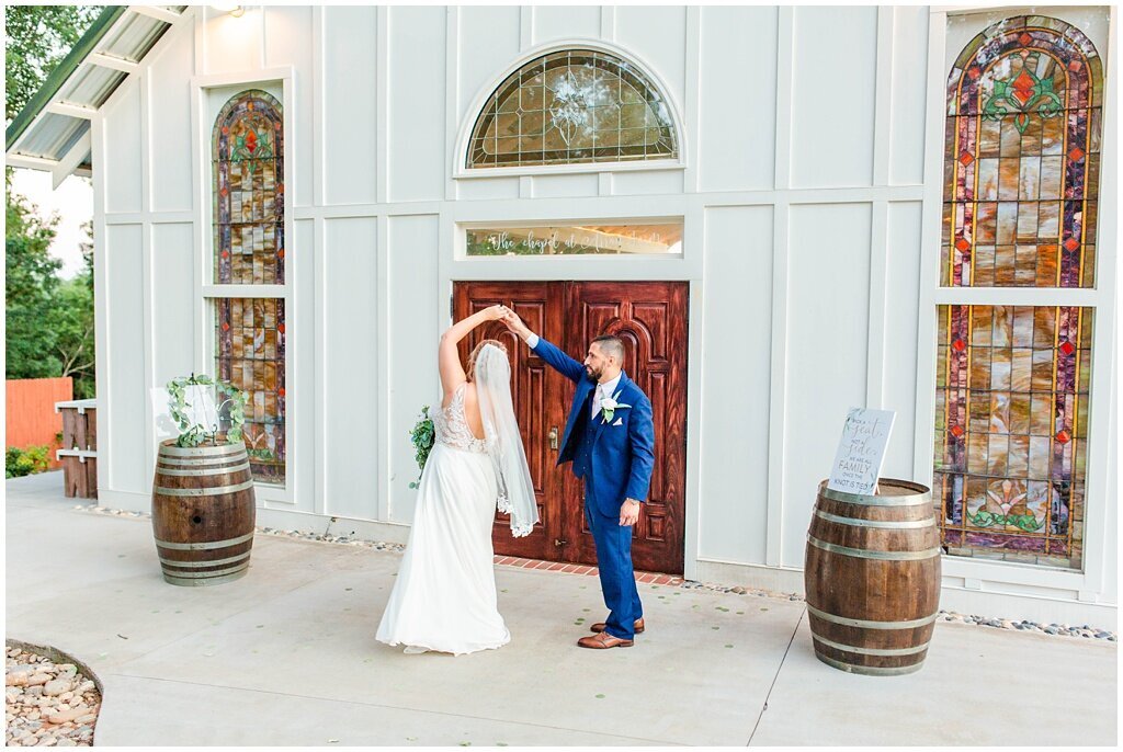 groom twirling bride in front of wedding chapel