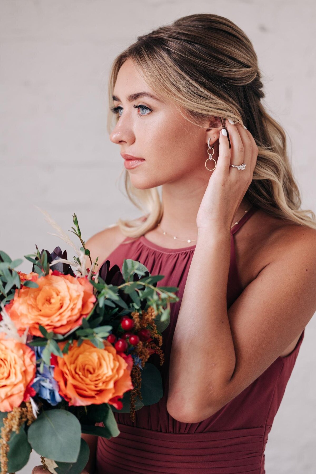 Woman in a burgundy dress holding a bouquet and adjusting her earring.