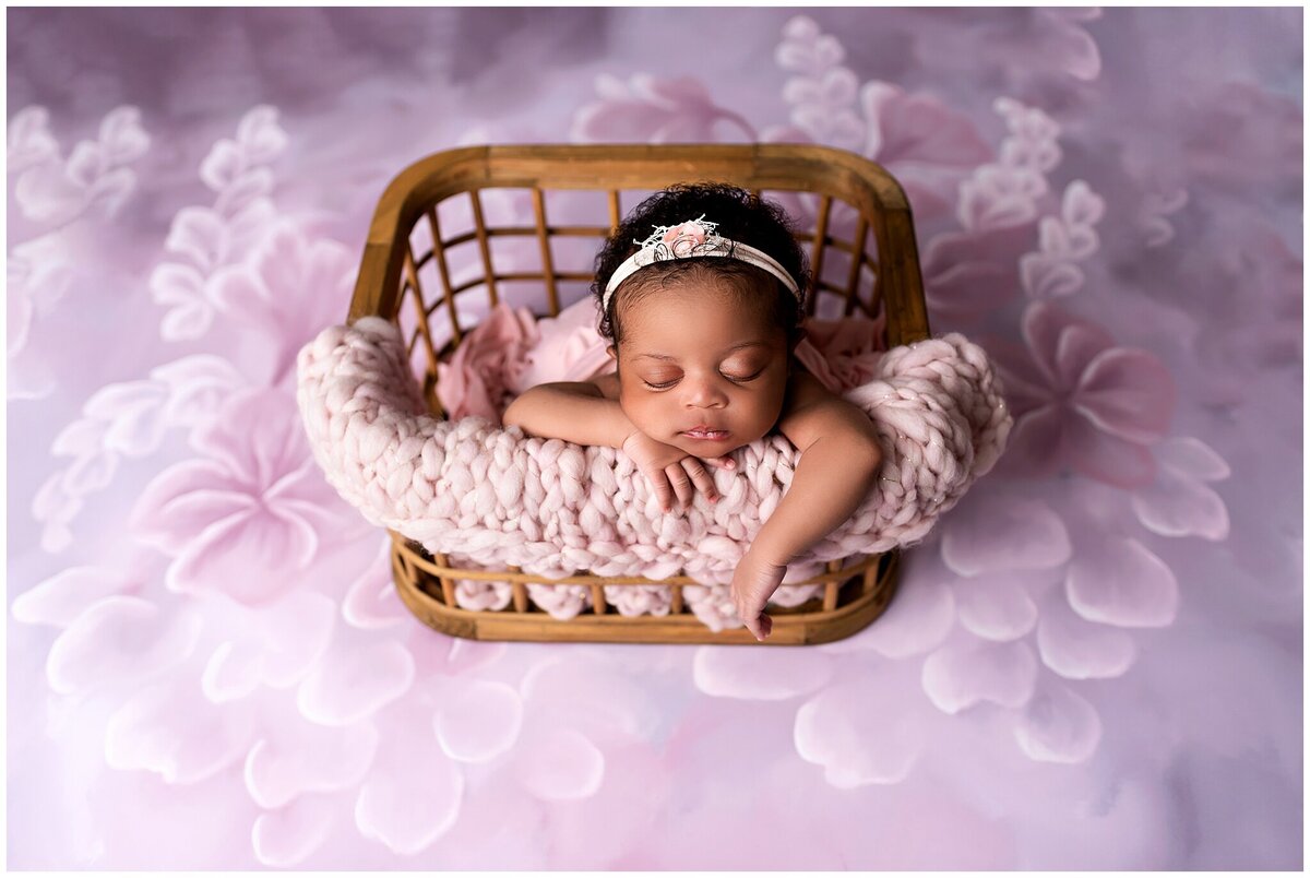 newborn girl laying in wooden basket with hands hanging off