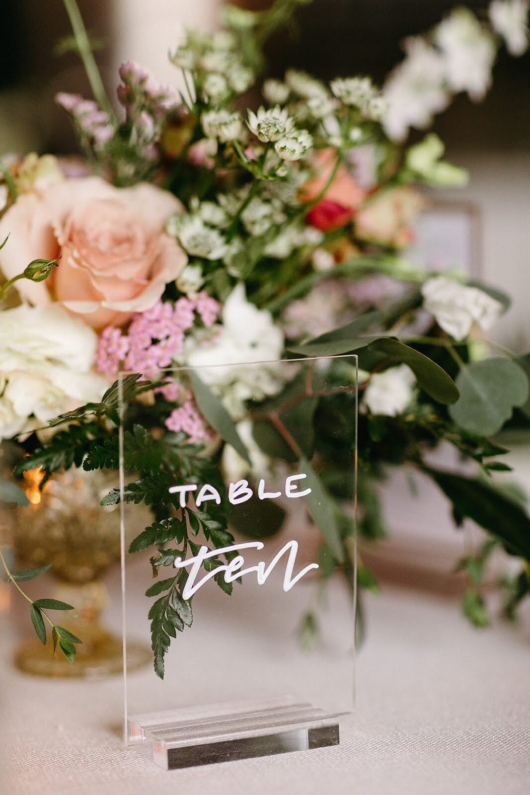 Custom wedding table ten sign with lush floral arrangement by Flowers and Thyme in the background.