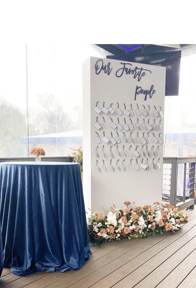 White seating chart backdrop design with name tags and floral arrangements on the ground