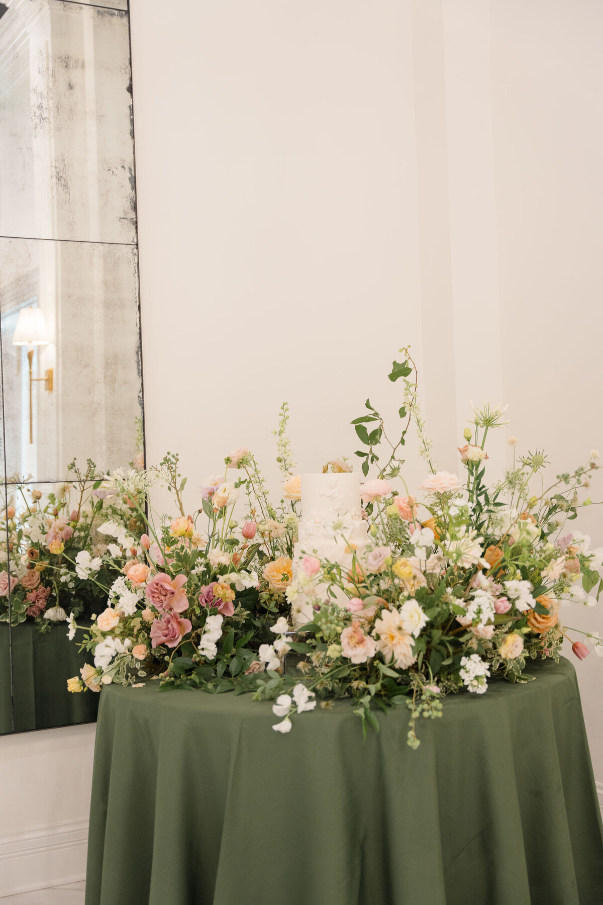 Floral display with white cake on green tablecloth.