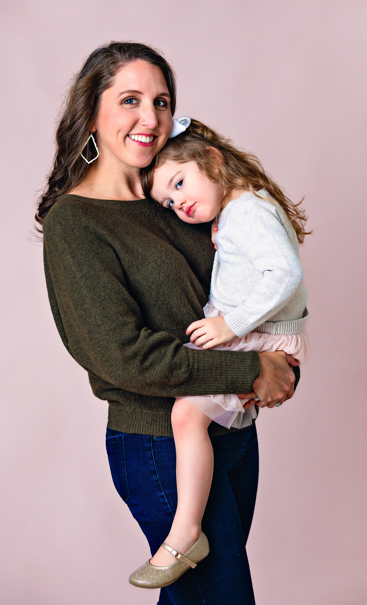 A mom in a green sweater is holding her young daughter as they pose for their studio session with Ashley Zohil Photography.