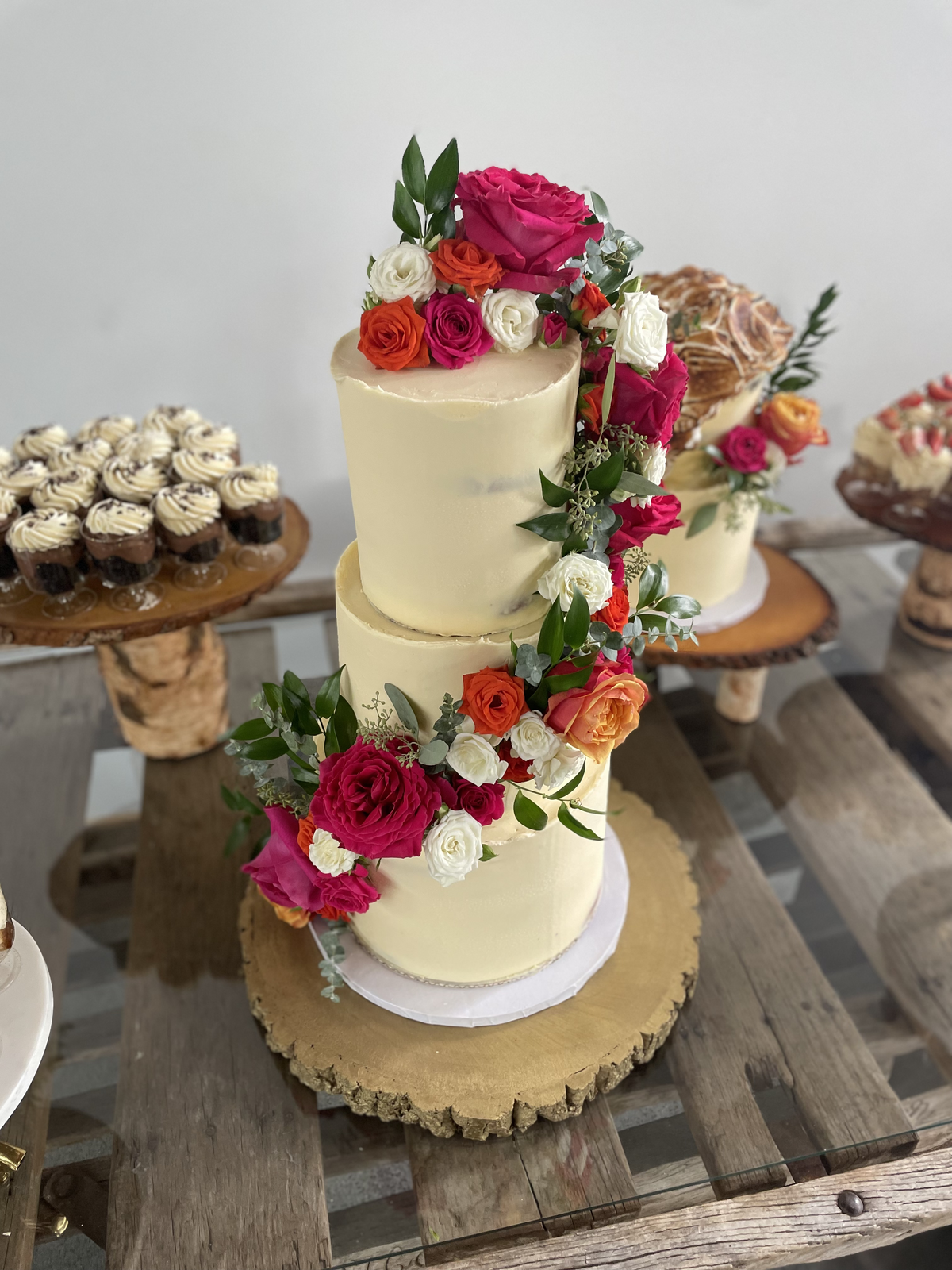 Two-tier gluten-free wedding cake adorned with a cascading arrangement of bright pink and red flowers, created by Grain Artisan Bakery in Snohomish, Washington.
