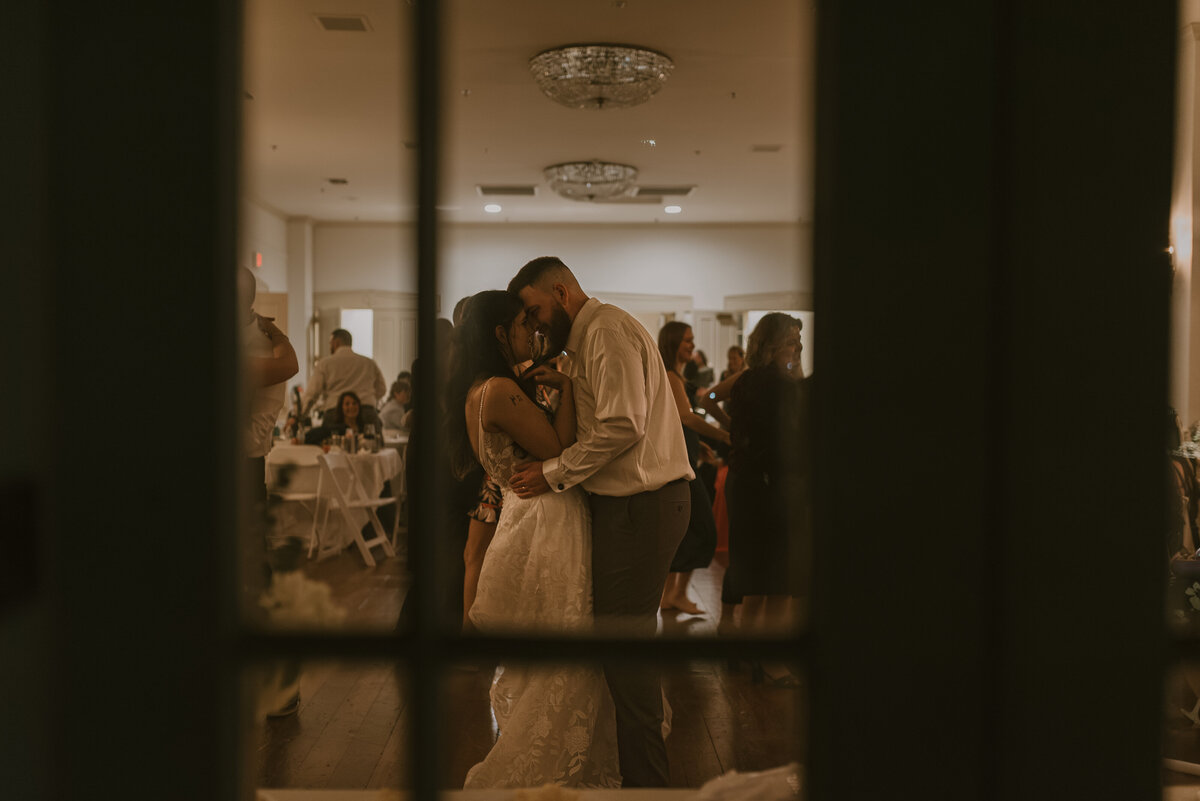 a window view of a wedding couple dancing at their reception.