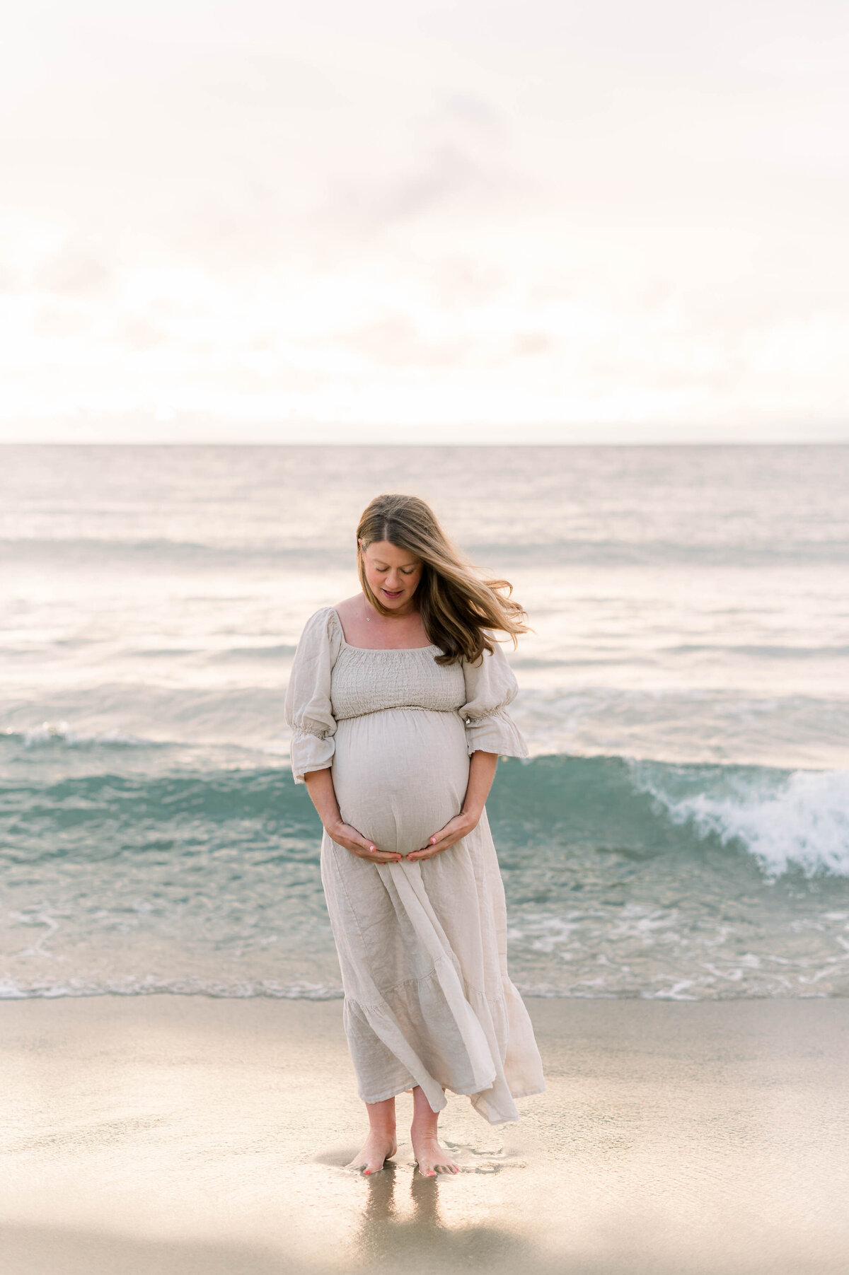 A pregnant woman standing on the beach in front of a beautiful wave while taking maternity photos.