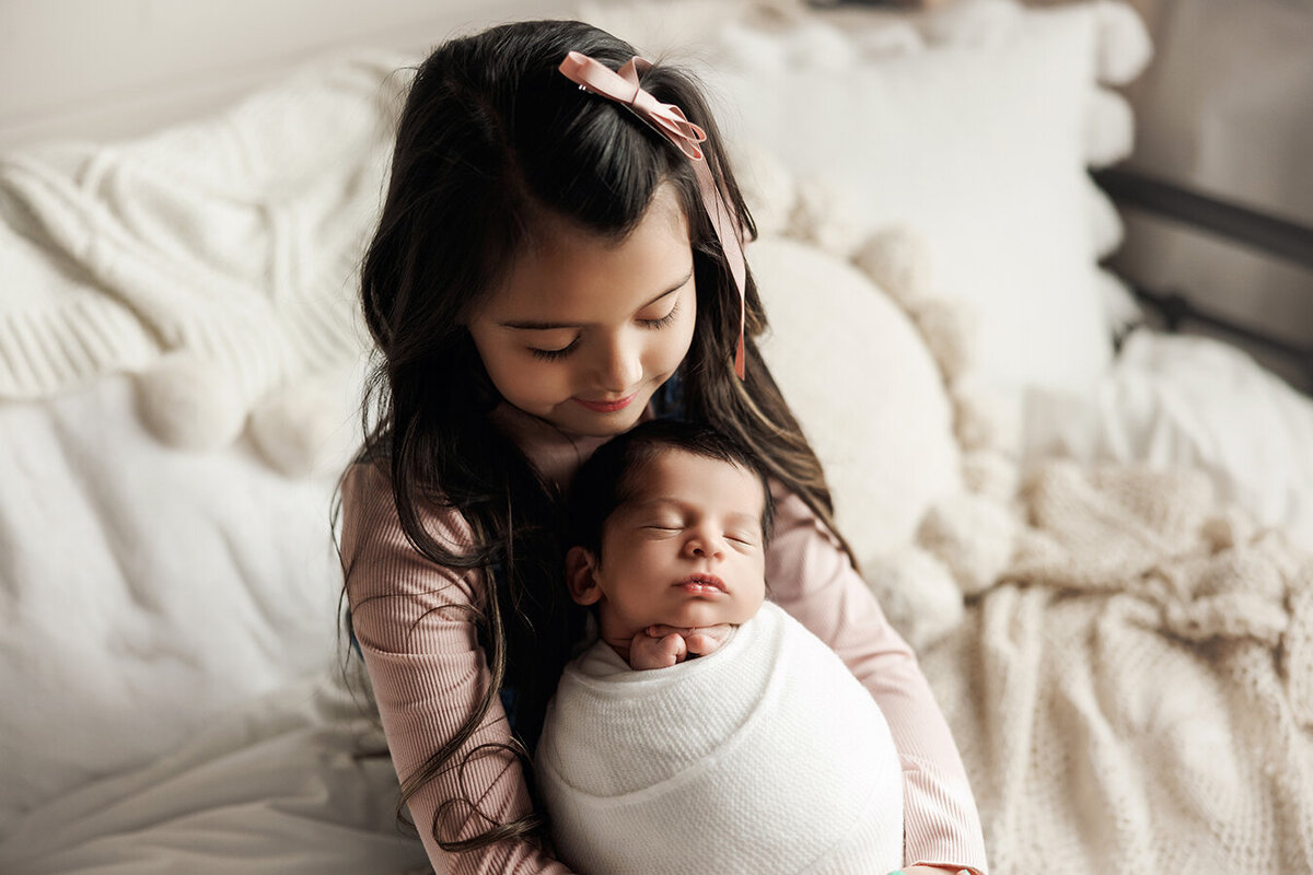 Gorgeous older sister holding newborn baby brother in window light