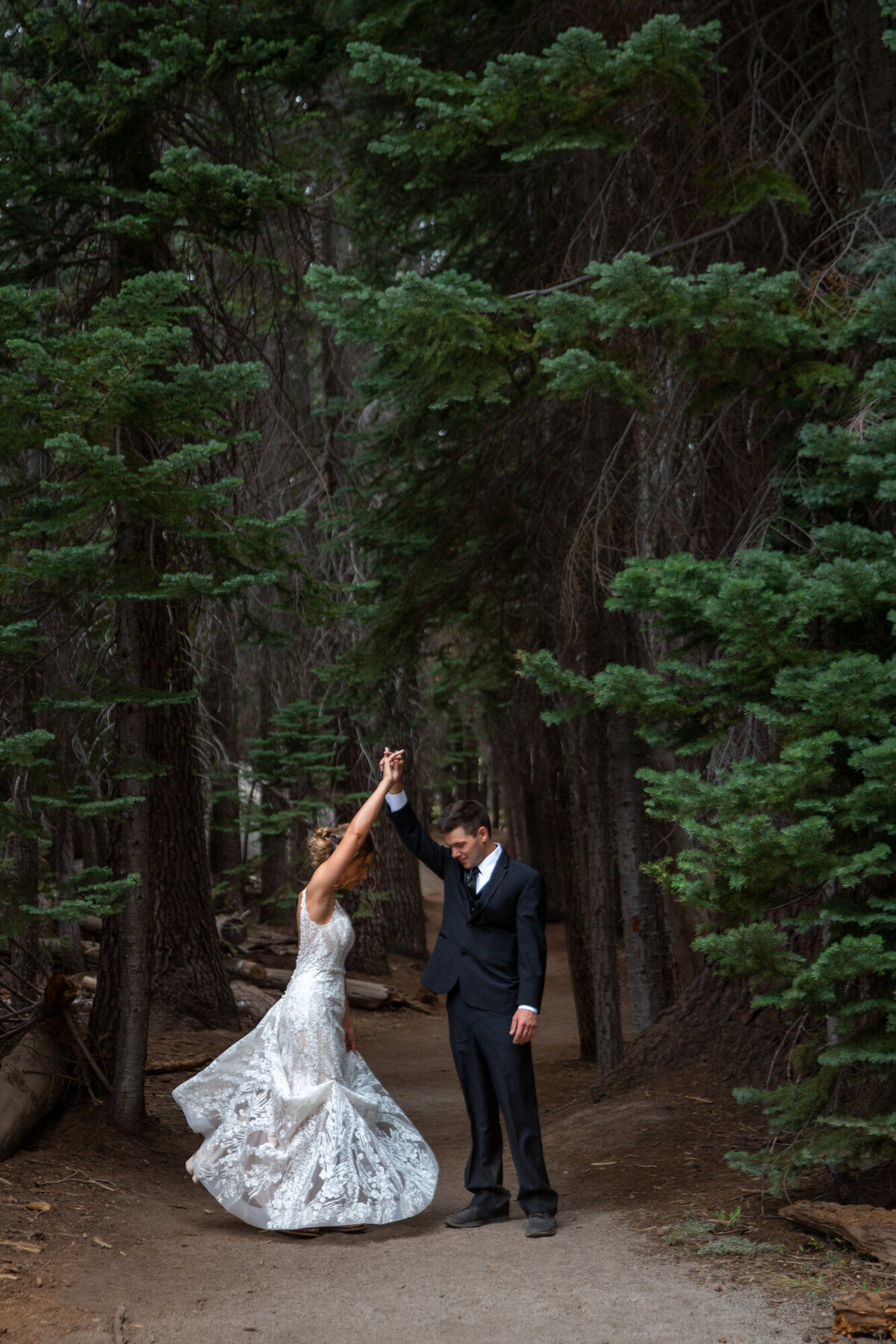 A groom twirls his bride as they stand in a grove of trees.